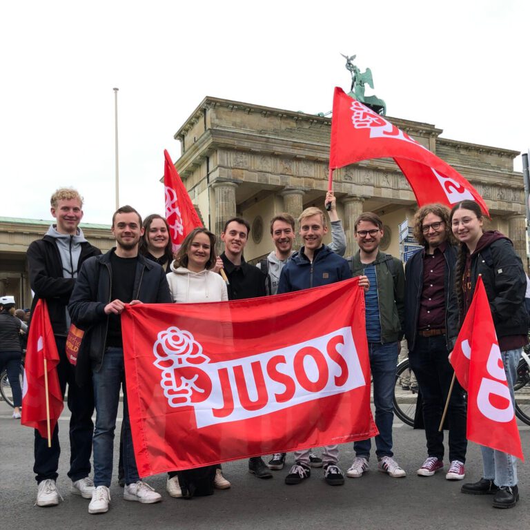 Gruppenbild der Jusos Friedrichshain-Kreuzberg mit Flaggen vor dem Brandenburger Tor am Arbeitskampftag 2022